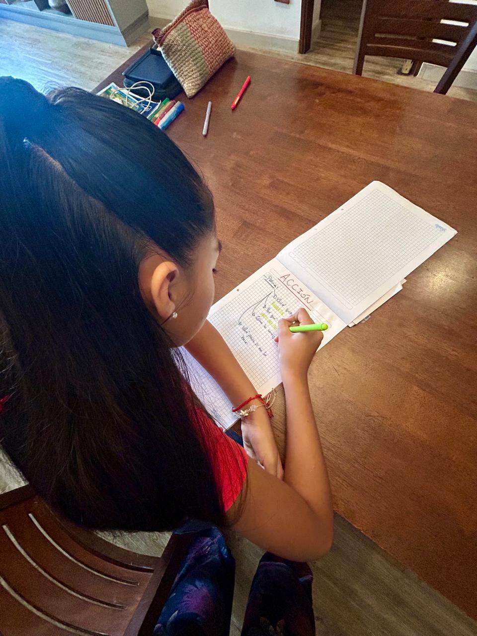 Niña escribiendo la palabra Acción en su cuaderno